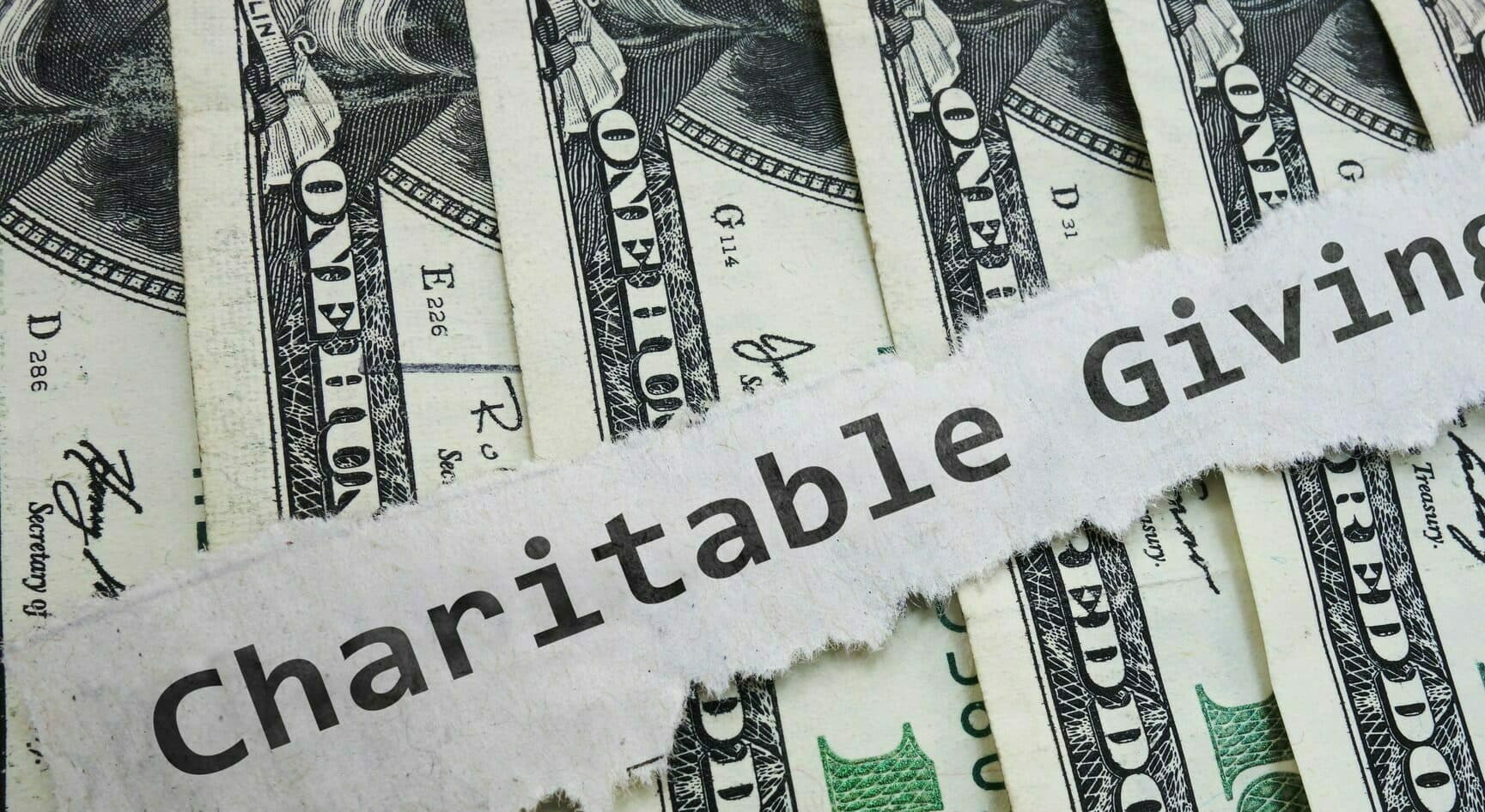 Charitable Contribution paper message on hundred dollar bills, representing the use of Qualified Charitable Distributions (QCDs)