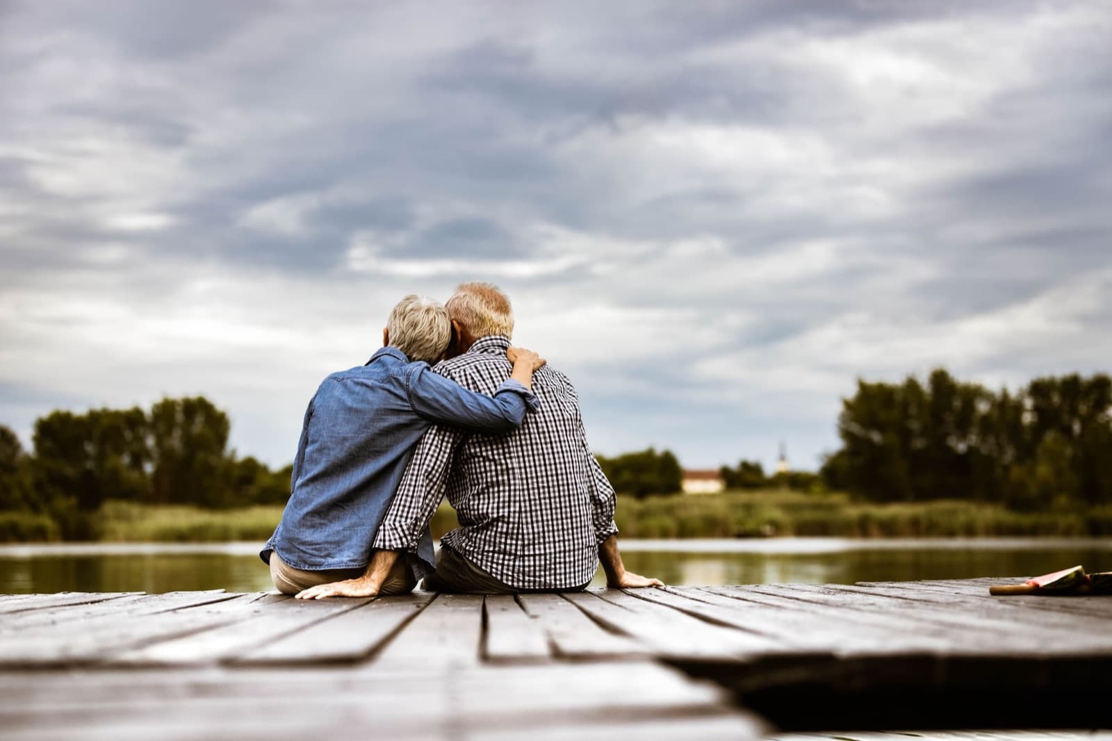 A senior couple sitting together at the end of a lake pier