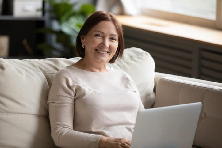 Older woman sitting on sofa with her laptop, representing retirement planning by Peterson Wealth Advisors